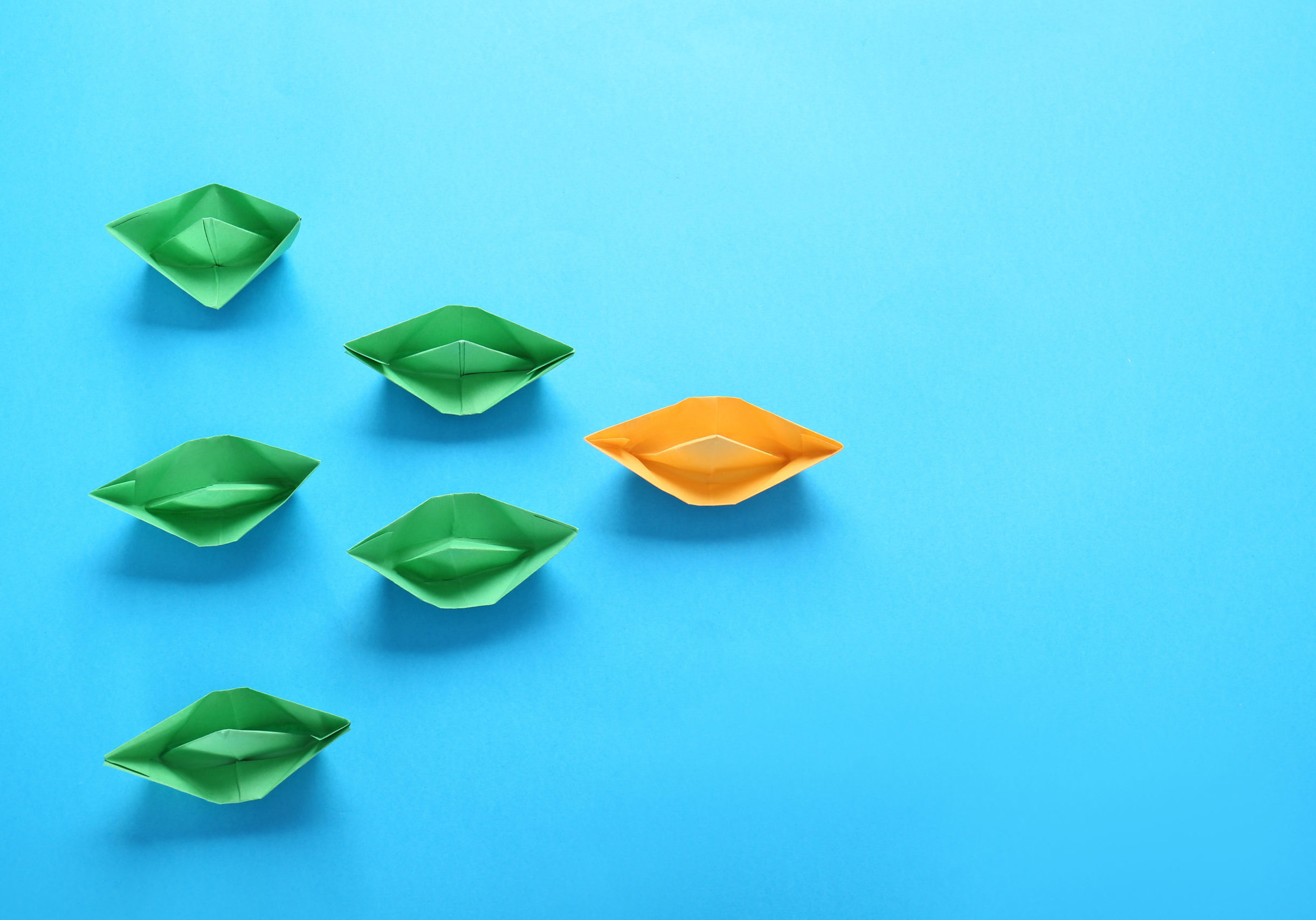 Orange origami boat among green ones on color background. Concept of uniqueness Orange origami boat among green ones on color background. Concept of uniqueness