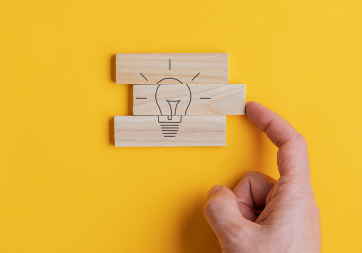 Conceptual image of vision and idea Wide view image of male hand assembling a light bulb drawing on wooden pegs in a conceptual image. Over yellow background.